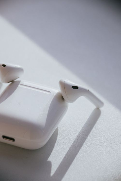 Free Close-up of wireless earphones and charging case on a white surface with natural light and shadows. Stock Photo