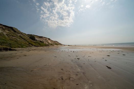 Peaceful sandy beach with dramatic cliffs under a blue sky, perfect for nature lovers.