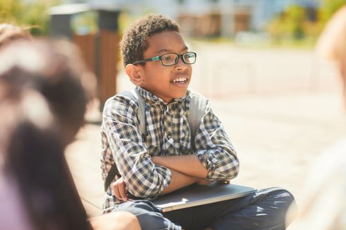 Free Smiling young boy sitting outdoors with a laptop on a sunny day. Stock Photo