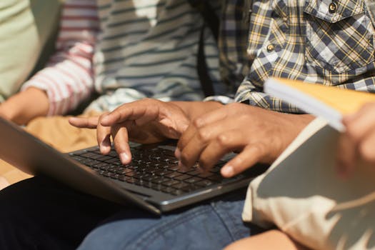 A diverse group of people using a laptop outdoors, focusing on hands and collaboration.