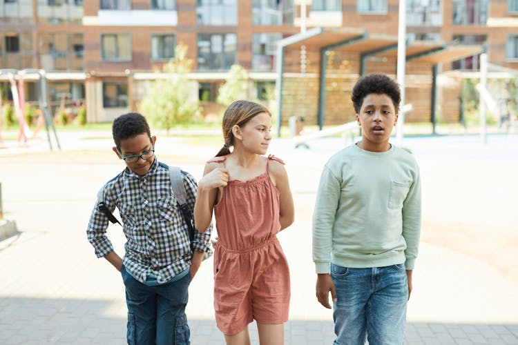 A Girl In Pink Romper Walking Between Boys