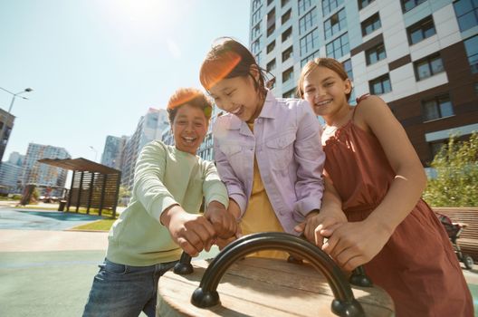 Diverse group of children laughing and playing outdoors in a city playground.