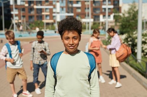 A Boy Smiling at the Camera while Standing Near Busy Students on His Back