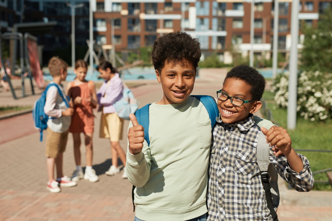 Deux amis souriants avec leur sac à dos devant leur école