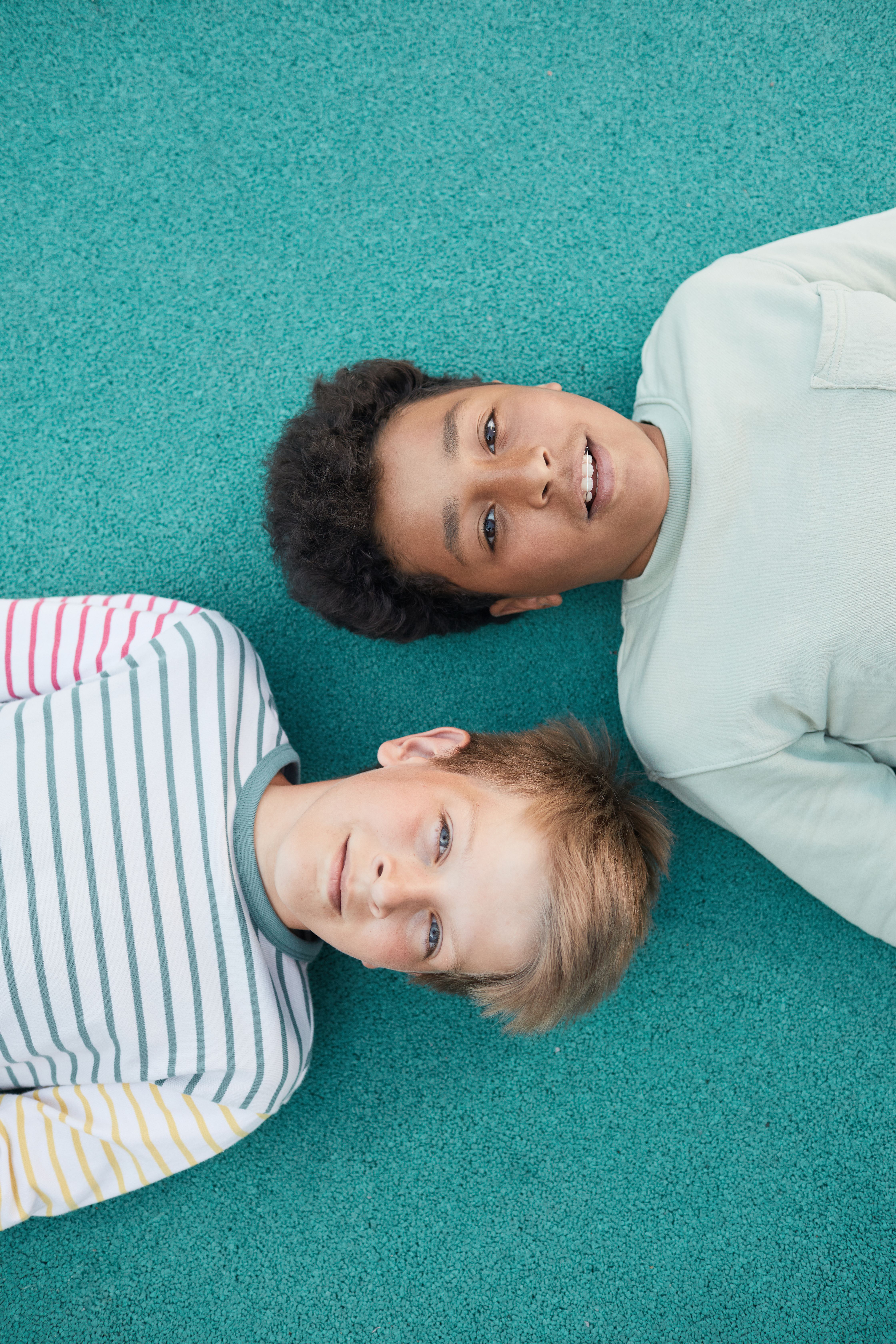 Two boys lying on a green surface, representing friendship and diversity, top view.