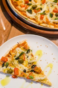 白色盘子上有一块美味披萨的特写镜头，上面配有奶酪、橄榄和西红柿等配料