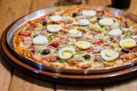 木桌上特写着一份美味披萨，上面有鸡蛋、火腿和橄榄