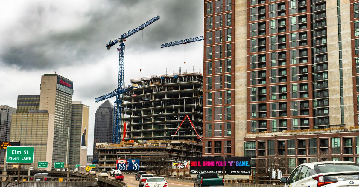 An active construction site with cranes surrounded by skyscrapers under cloudy skies in a bustling city.