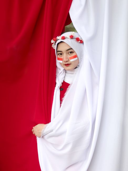 A young woman wearing traditional Indonesian clothing with face painted red and white, symbolizing the Indonesian flag.