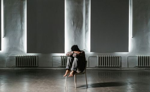Free A solitary figure sits on a chair in an empty, dimly lit room, reflecting solitude and introspection. Stock Photo