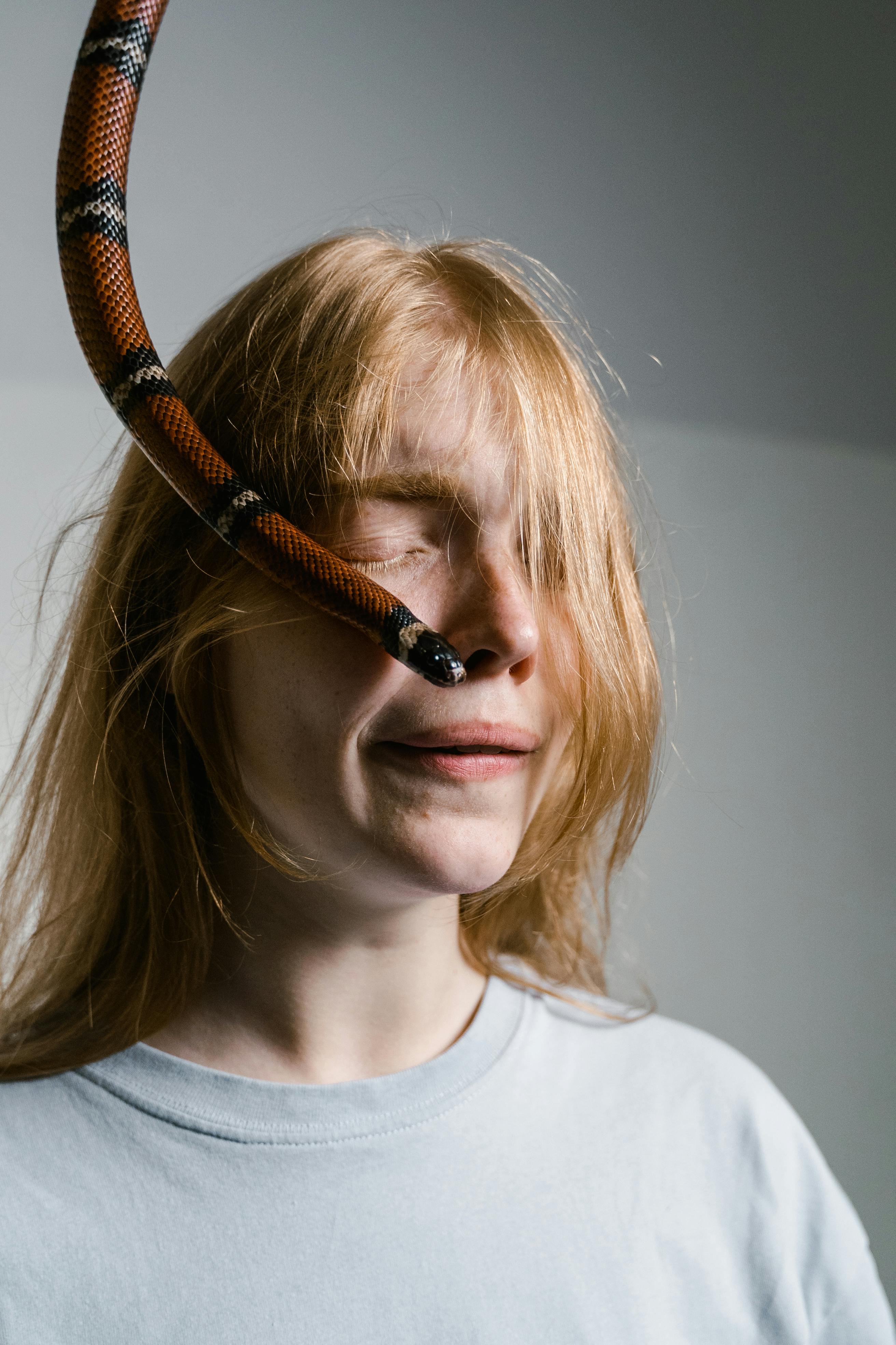 Close-up of woman confronting fear, snake draped over face, evoking themes of anxiety and bravery.