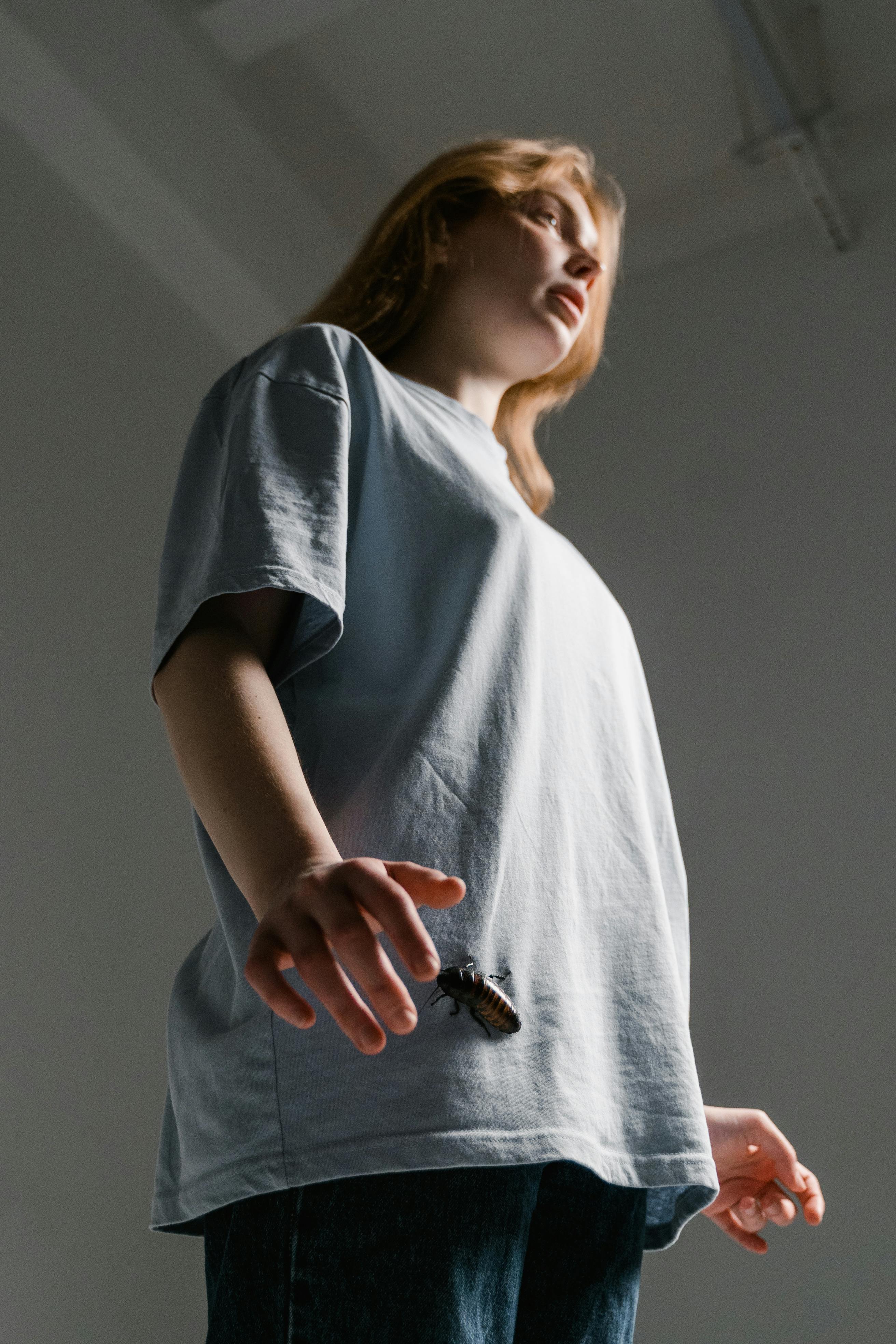 A woman stands indoors with a cockroach on her hand, capturing a moment of anxiety and fear.