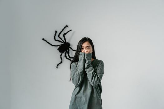 A woman looking anxious with a large spider on the wall behind her, illustrating arachnophobia.