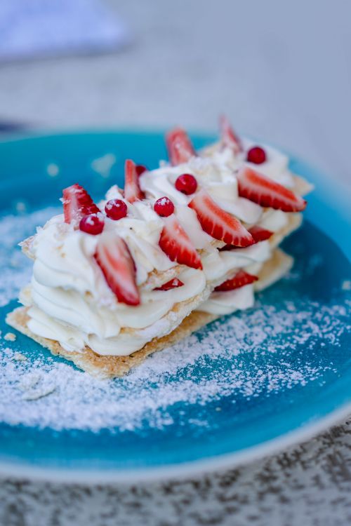 Free A creamy dessert layered with fresh strawberries and whipped cream on a blue plate. Stock Photo