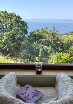 Relaxing ocean view through a cozy window with journal and drink setting.