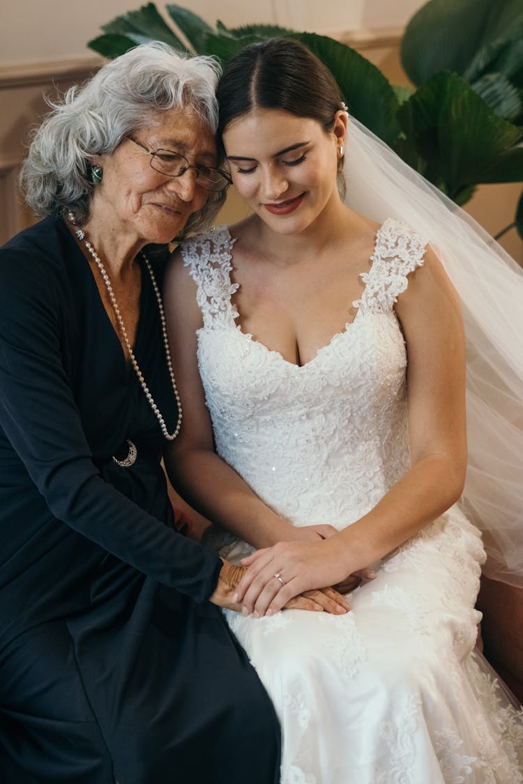 An Elderly Woman In Black Long Sleeve Dress Sitting Beside The Bride In White Wedding Dress