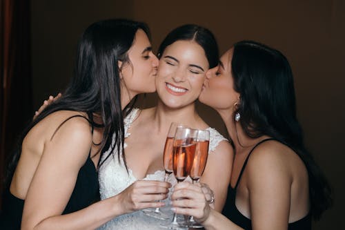 Free Two Women Kissing the Bride while Holding Champagne Glasses Stock Photo