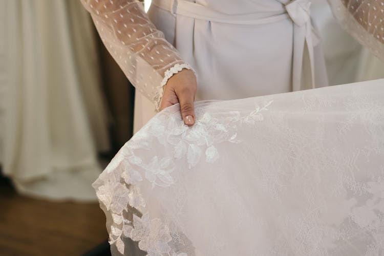 A Person Holding A White Floral Lace Wedding Dress