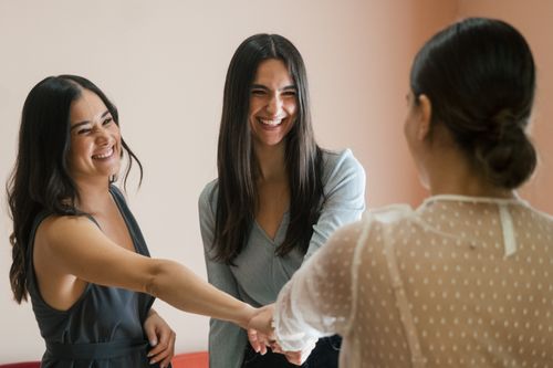Free Three women joyfully stacking hands indoors, symbolizing friendship and togetherness. Stock Photo