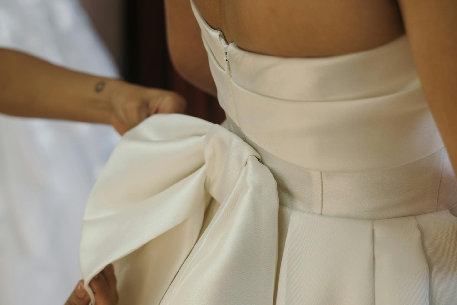 Elegant close-up of a white bridal dress bow being adjusted during a wedding preparation.