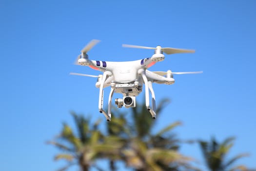 Aerial drone with camera flying against a blue sky backdrop, palm trees below.