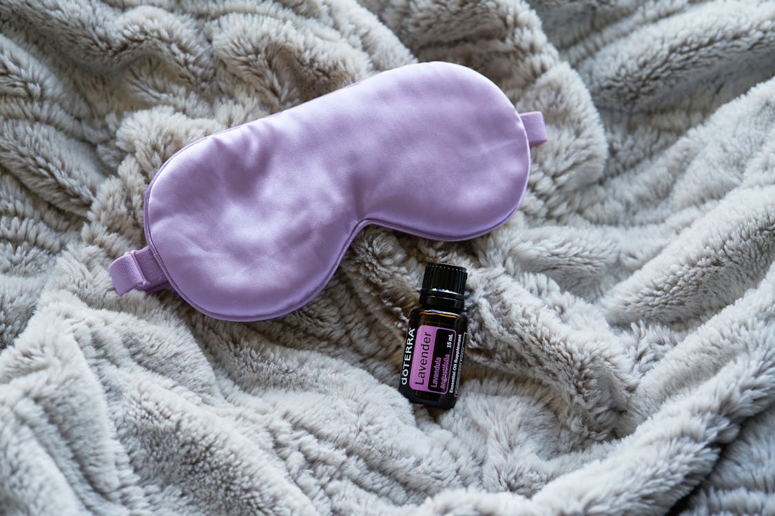 Free Purple Sleep Mask Beside Small Plastic Bottle on Gray Blanket Stock Photo