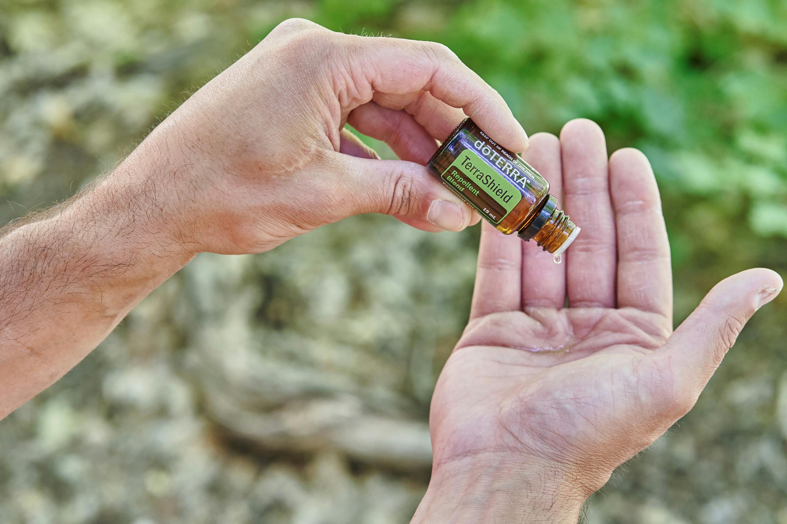 a person holding a small glass bottle while dripping oil on it s hand