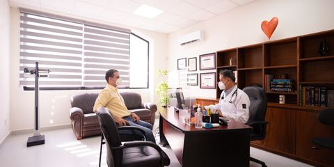A patient consults with a masked doctor in a well-lit, modern office. Safety measures in place.