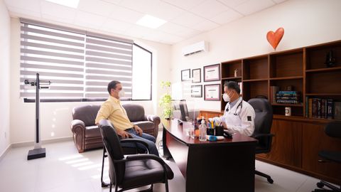 A patient consults with a masked doctor in a well-lit, modern office. Safety measures in place.