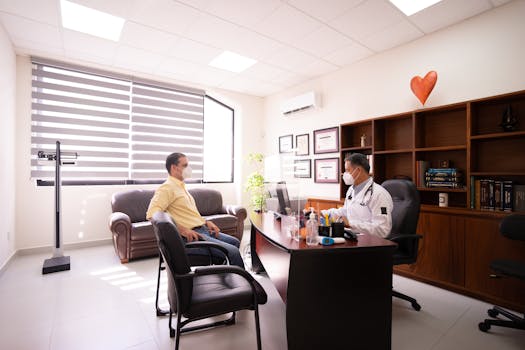 A patient consults with a masked doctor in a well-lit, modern office. Safety measures in place.