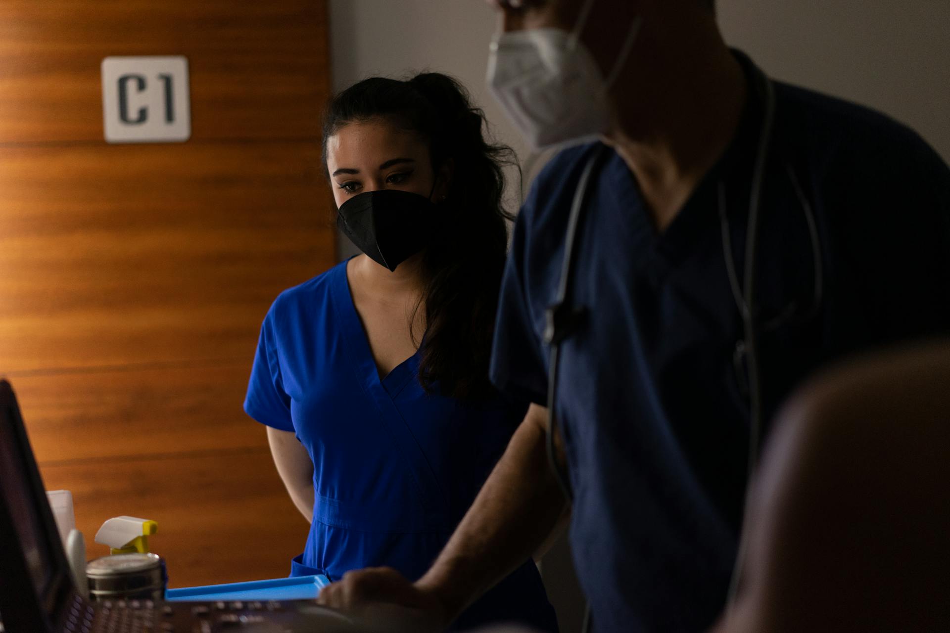 Doctors in scrubs and masks examining patient data in a hospital room.