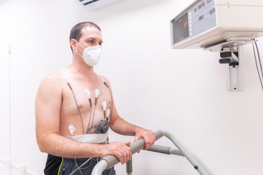 Man in medical exam wearing electrodes and face mask performing heart stress test on treadmill.