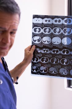 A male doctor in scrubs examines an X-ray scan in a clinical setting, focusing on the patient's chest area.