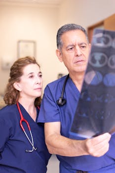Two healthcare professionals in scrubs examine an x-ray image in a hospital setting.