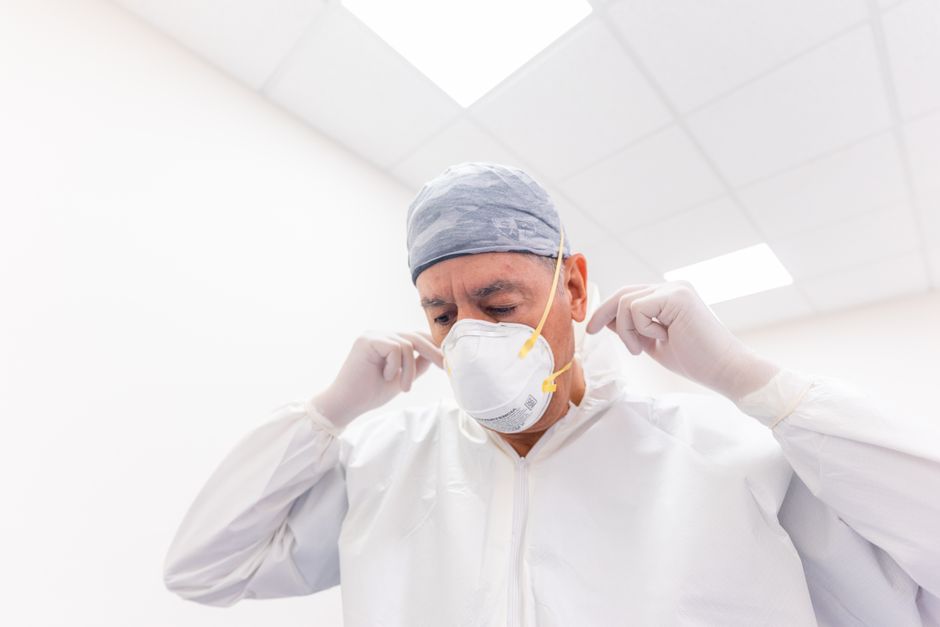 Male healthcare professional adjusting face mask and PPE in a hospital setting.