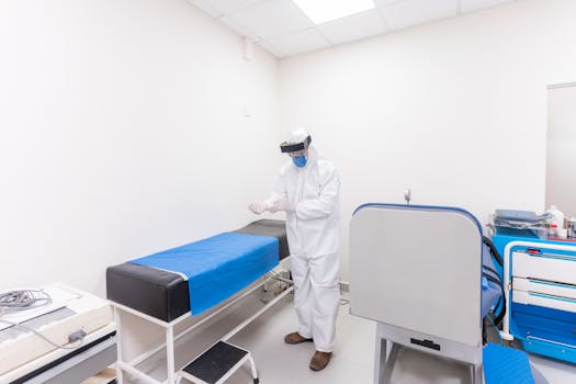 A healthcare worker in full PPE readies for work in a well-equipped hospital room.