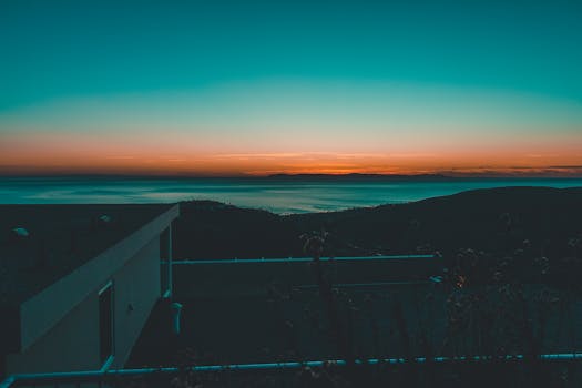 A breathtaking sunset view over calm ocean waters with silhouetted hills in the foreground.