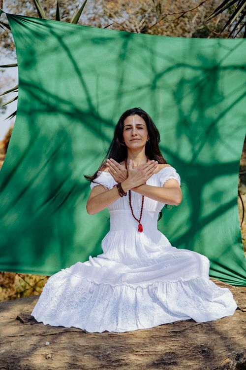 Free Woman meditating outdoors on rock with green backdrop and shadows. Stock Photo
