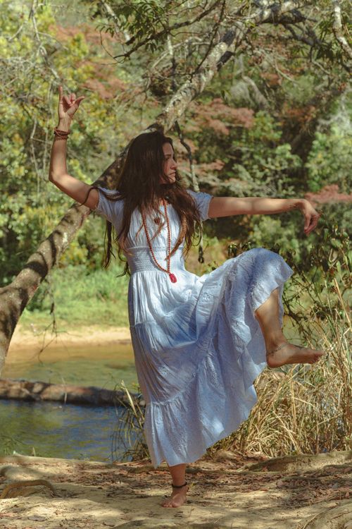 Free Woman in white dress dancing gracefully in a forest setting by a river. Stock Photo