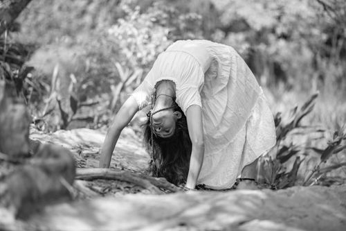 Free A woman in a white dress performing a yoga pose outdoors in a black and white forest setting. Stock Photo