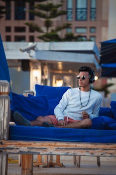 Stylish young man relaxing on a bench in Essaouira, Morocco, wearing headphones and sunglasses.