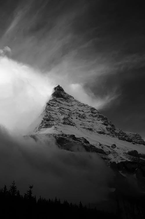 Grayscale Photo of Snow Covered Mountain under a Cloudy Sky