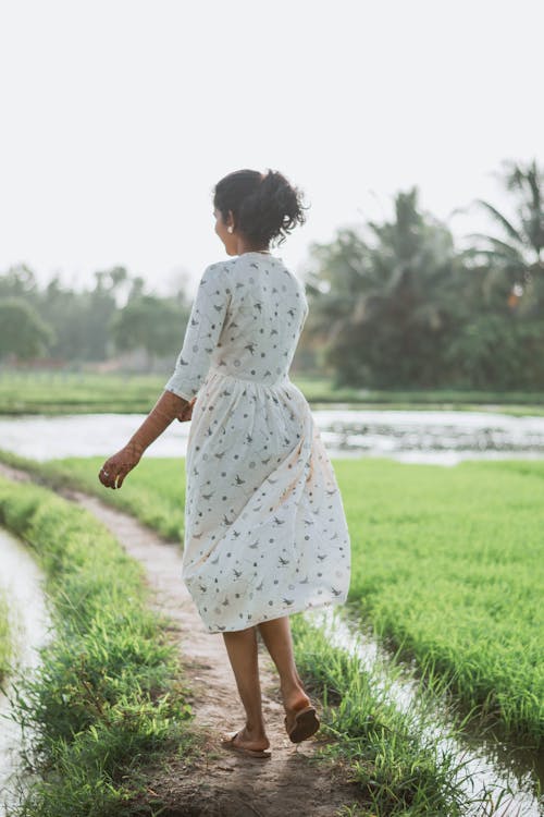 Back View of a Woman in a White Dress Walking in a Farm