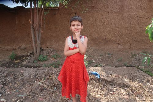 Free A young girl in a vibrant red dress posing confidently outdoors against a wall. Stock Photo