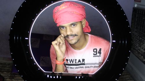 Free A cheerful man with a pink turban smiles at the camera through a ring light. Stock Photo