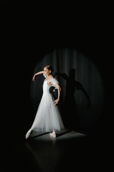 A graceful ballerina performs under spotlight in a studio, showcasing elegance and skill.