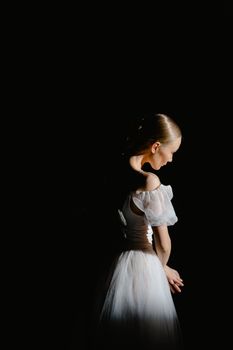 A graceful ballerina in a white dress poised under a dramatic spotlight, showcasing elegance and artistry.