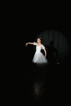 A graceful ballerina performing solo under a spotlight in a dark studio.