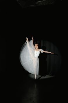 Ballerina in white dress dances elegantly under spotlight, showcasing poise and grace.