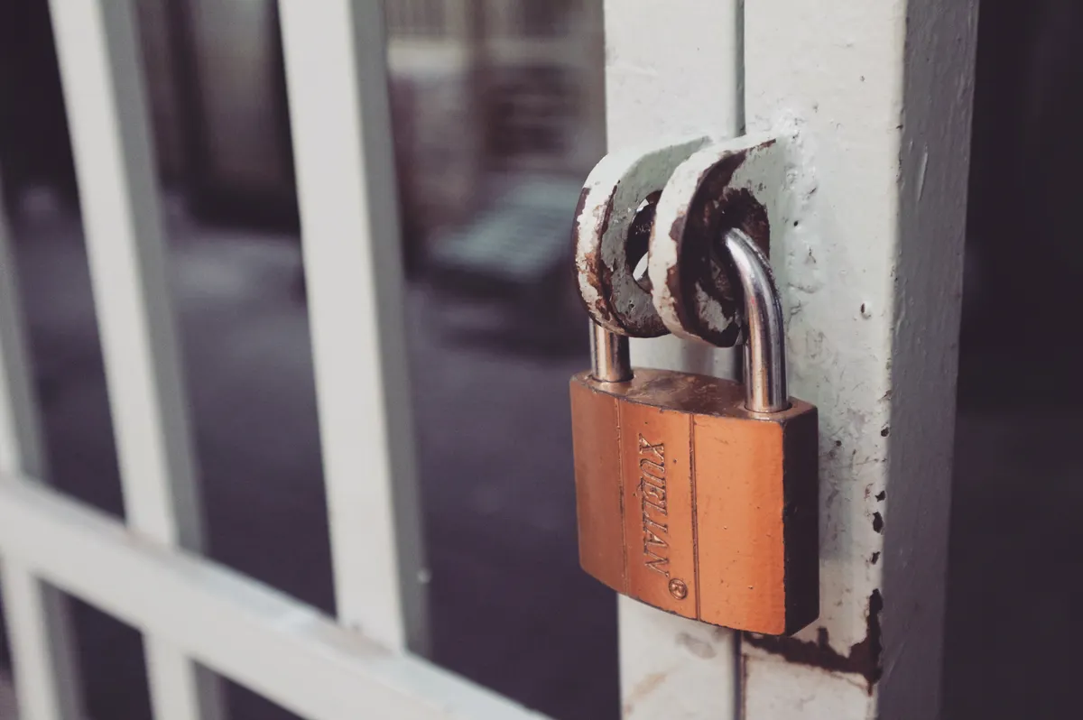 A brass padlock hanging from a latch on a weathered white gate.